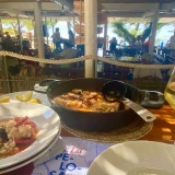 A pan and bowl of Catalan seafood rice with a glass of white wine